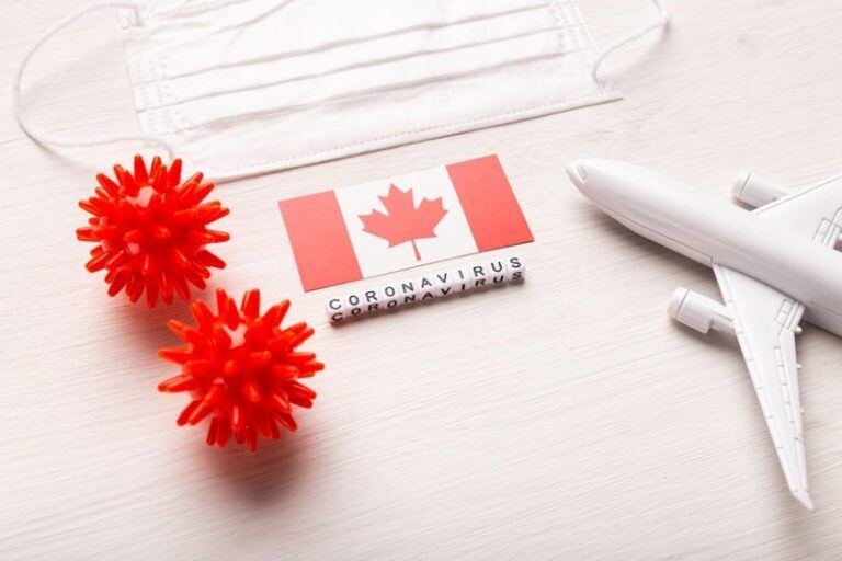 canada flag with an airplane and facemask on a table and a corona virus word and symbol