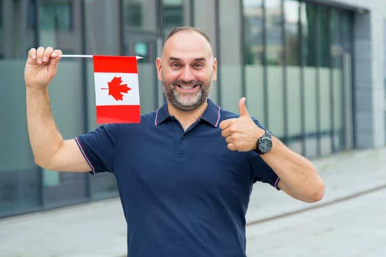 Excited new immigrant giving thumbs up & holding a Canadian flag