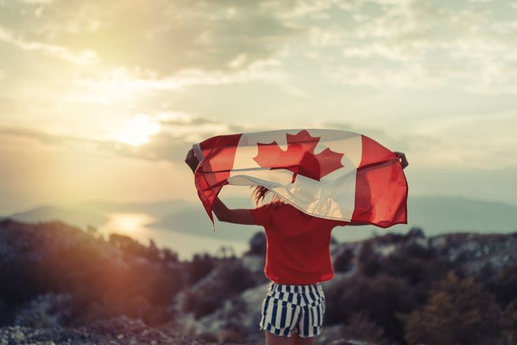 Canadian citizen waving Canada flag on hilltop at sunset